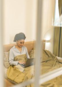 A woman sits in bed typing on her laptop