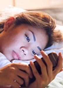 Girl scrolling on phone in bed