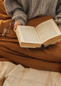 Woman reading book in bed with blanket